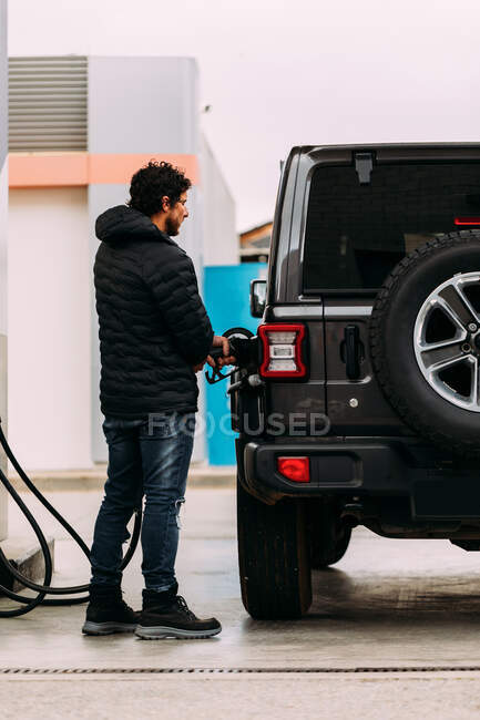 Vista lateral de un hombre repostando su coche todoterreno en una gasolinera - foto de stock