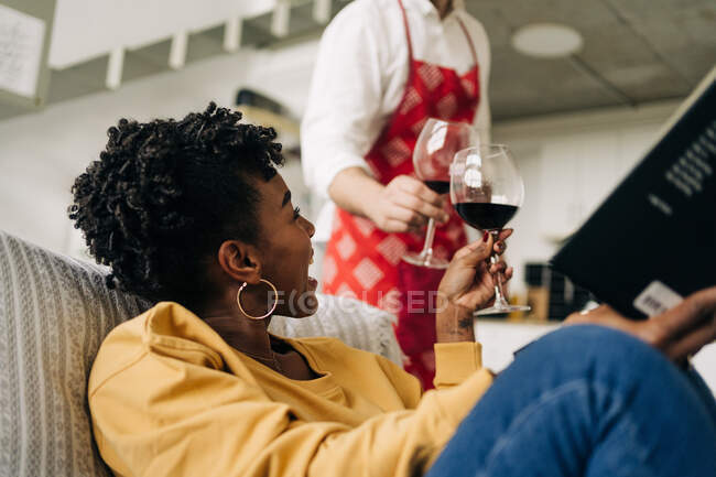 Baixo ângulo de casal multirracial clicando copos com vinho tinto enquanto desfruta de fim de semana em casa — Fotografia de Stock