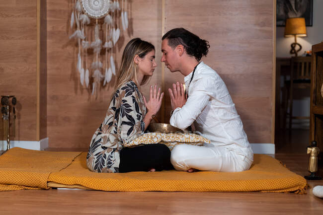 Visão lateral do professor Zen com o parceiro feminino sentado com pernas cruzadas e olhos fechados durante a prática espiritual — Fotografia de Stock