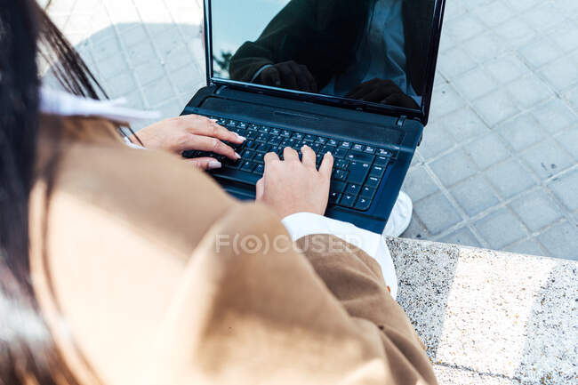De cima cortado fêmea irreconhecível sentado no banco na estação ferroviária e laptop de navegação enquanto espera por trem — Fotografia de Stock
