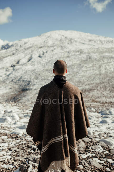 Vue arrière d'un touriste masculin anonyme admirant une montagne enneigée sous un ciel nuageux bleu en hiver — Photo de stock