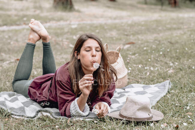 Carefree female lying on blanket in woods and blowing dandelion while enjoying picnic in Australia — Stock Photo