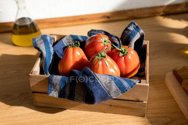 Alto ángulo de tomates rojos maduros frescos colocados en bandeja de madera natural con servilleta en la cocina casera - foto de stock