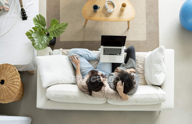 From above of anonymous couple with netbook interacting on sofa against cups of tea at home — Stock Photo