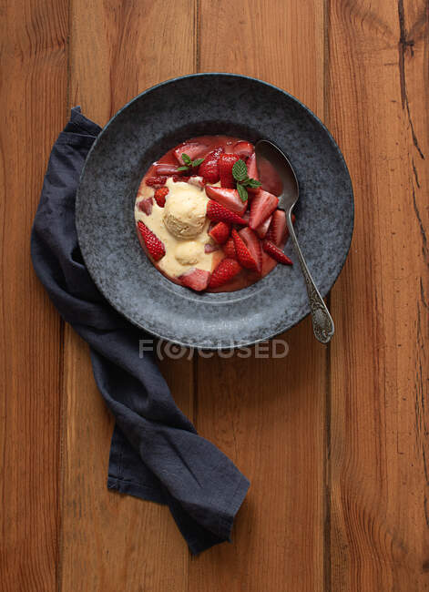 Vista superior de saborosas metades de morango inflamado com sorvete de baunilha em placa na mesa de madeira — Fotografia de Stock