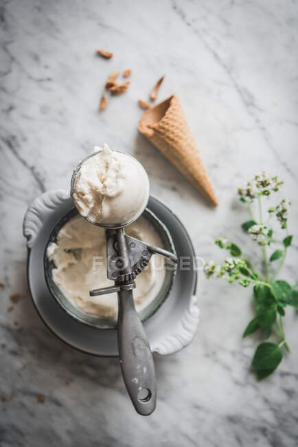 Desde arriba de cono de gofre cerca de merengue cucharadas de helado de leche y hojas de menta fresca en la mesa de mármol - foto de stock