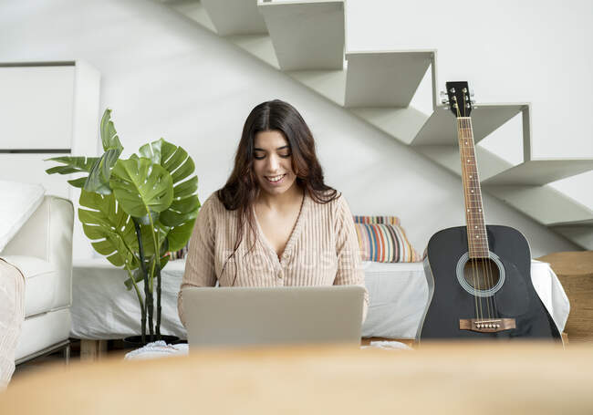 Молода щаслива жінка переглядає Інтернет на портативному комп'ютері проти рослин і сходів в домашній кімнаті — стокове фото