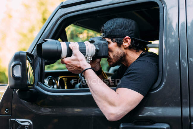Vista lateral de um fotógrafo aventureiro tirando fotos de dentro de seu carro off-road — Fotografia de Stock