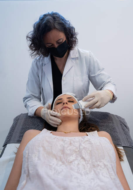 Cosmetologo professionista che fa peeling viso ad ultrasuoni per donna rilassata sdraiata sul tavolo medico nella moderna clinica di bellezza — Foto stock