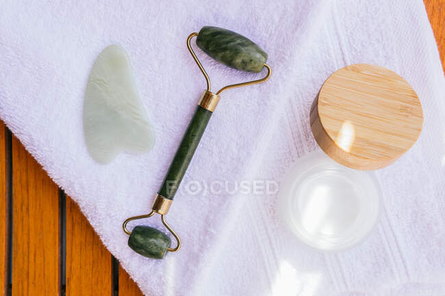 High angle of jade roller and guasha scraper placed on wooden table with towel and natural facial cream in spa salon — Stock Photo