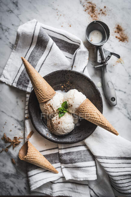 De arriba de los conos de gofre con merengue cucharadas de gelato de leche y hojas frescas de menta con canela en polvo en la parte superior - foto de stock