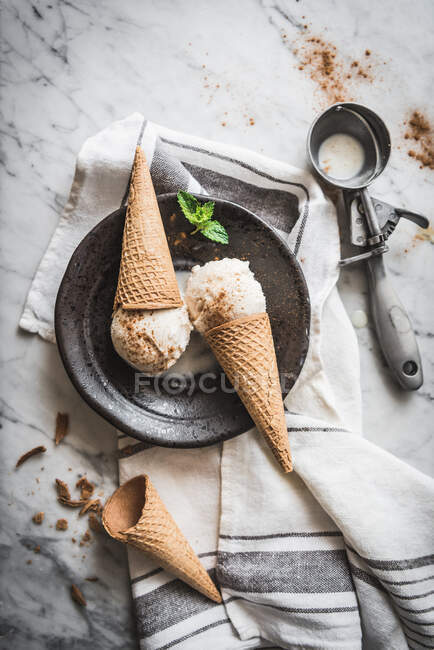 De arriba de los conos de gofre con merengue cucharadas de gelato de leche y hojas frescas de menta con canela en polvo en la parte superior - foto de stock