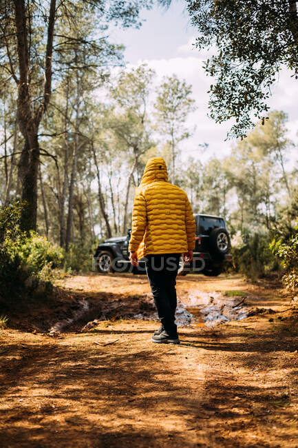 Back view of hooded adventurer posing next to his off-road car on the road — Stock Photo