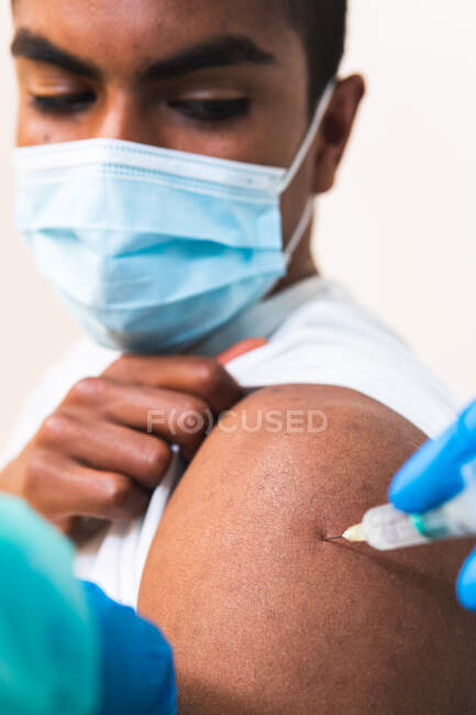 Ritagliato specialista medico femminile irriconoscibile in uniforme protettiva, guanti in lattice e maschera facciale vaccinare paziente uomo afroamericano in clinica durante l'epidemia di coronavirus — Foto stock