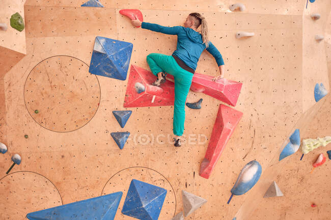 Atleta feminina escalando parede artificial durante o treino de pedregulho no ginásio profissional — Fotografia de Stock