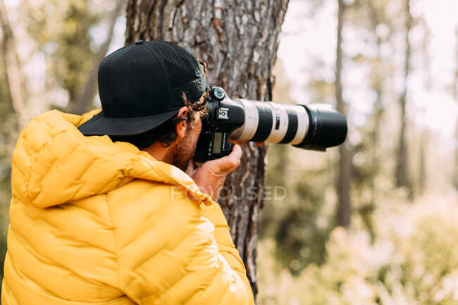 Vista lateral de um fotógrafo aventureiro tirando fotos na montanha com fundo embaçado — Fotografia de Stock