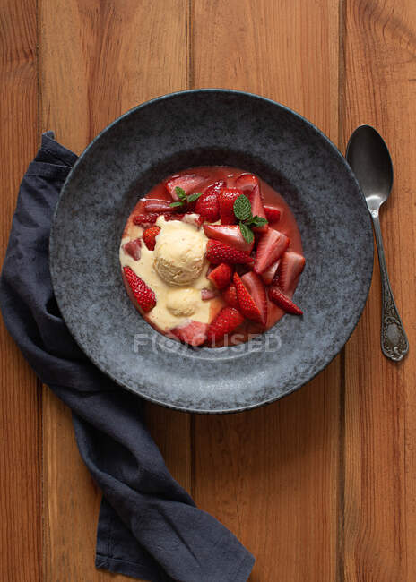 Top view of tasty flambeed strawberry halves with vanilla ice cream in plate on wooden table — Stock Photo