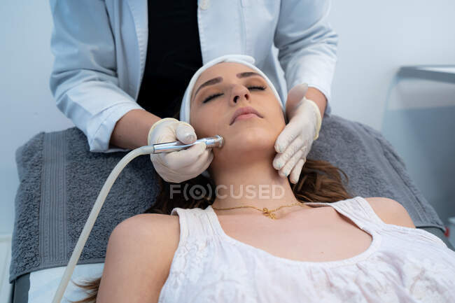 Нерозбірливий професійний косметолог за допомогою спеціального обладнання і мікродермабрація лицьовий бік жінки - клієнтки в сучасній клініці краси. — стокове фото