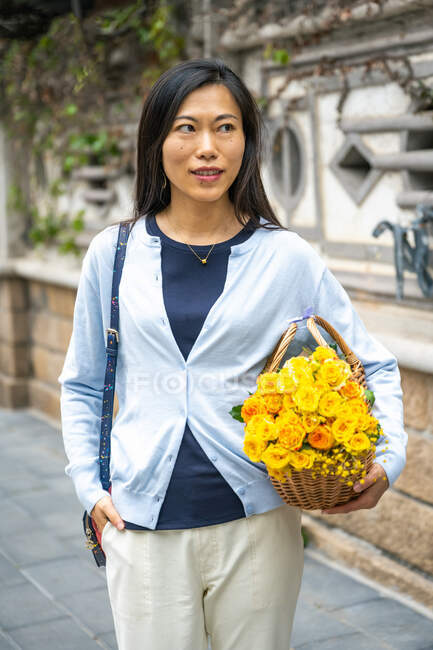 Bella ragazza asiatica ritratto mentre lei porta un cesto di vimini con fiori gialli. — Foto stock