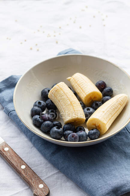 Du dessus du bol rond avec des bleuets mûrs et des bananes coupées pour le petit déjeuner — Photo de stock
