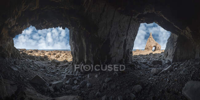 Грубый пещерный пейзаж острой скалы с отверстием на каменистом пляже Campiecho под голубым небом в Астурии — стоковое фото