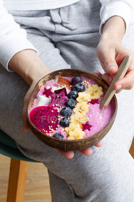 High angle of crop unrecognizable female with power bowl full of fresh banana and pitaya slices with smoothie and blueberries — Stock Photo