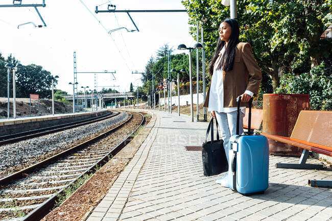 Vue latérale du voyageur asiatique avec valise debout sur le quai de la gare en attendant le train — Photo de stock