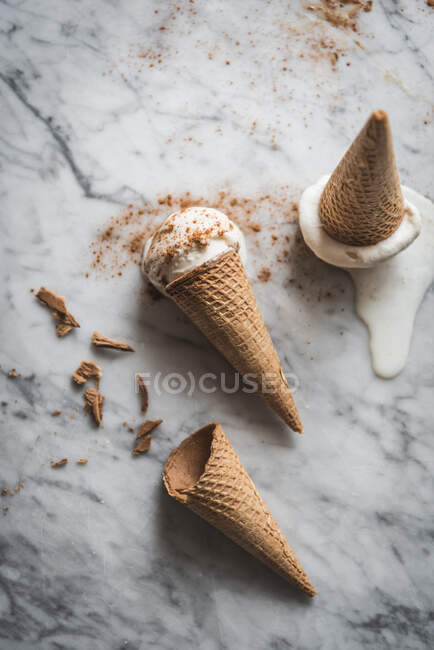 Vista aérea de sabrosos conos de gofre con cremosas cucharadas de gelato de leche merengue en la mesa de mármol - foto de stock