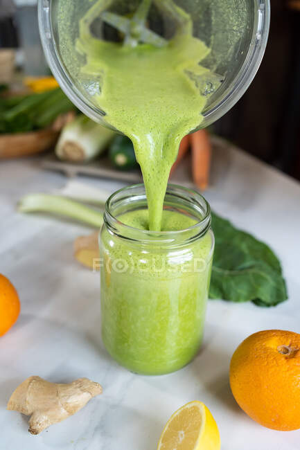Crop anonymous female pouring tasty smoothie from blender bowl into jar at table with citrus fruits at home — Stock Photo