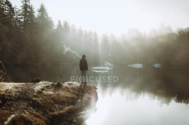 Анонимный человек стоит и смотрит на озеро в туманный день — стоковое фото
