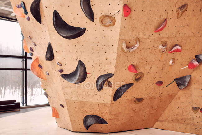 Parete artificiale squallida con impugnature da arrampicata situate in un luminoso e spazioso centro di boulder di giorno — Foto stock