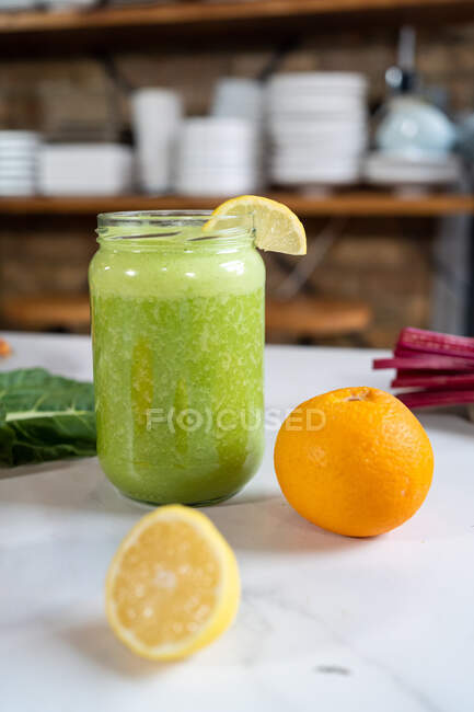 Банка вкусного здорового напитка на столе со свежим апельсином и лимоном на домашней кухне — стоковое фото