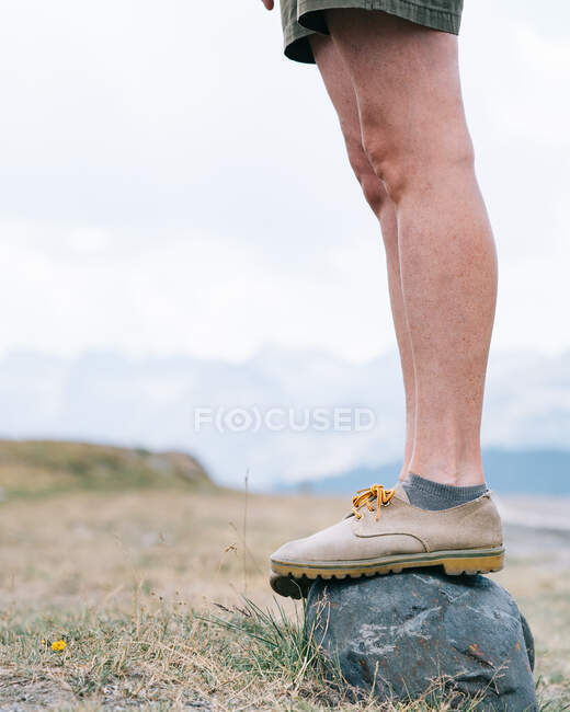 Вид сбоку на женщину-туристку в ботинках, стоящую на камне на природе во время похода летом — стоковое фото