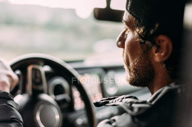 Vista lateral do homem barbudo dirigindo carro no fundo embaçado ao pôr do sol — Fotografia de Stock