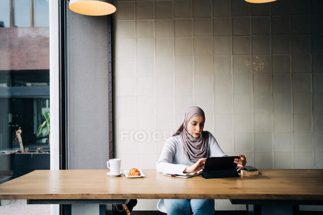 Зміст мусульманки в Хіджабі і розмови на відеочатах за планшетом, сидячи за столом у кафе. — стокове фото