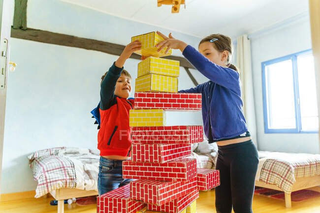 Vista lateral de los niños jugando al edificio con piezas de cartón en casa - foto de stock