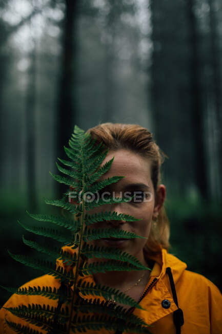 Adulto viajante feminino com folha de planta verde exuberante olhando para a câmera durante a viagem na floresta — Fotografia de Stock