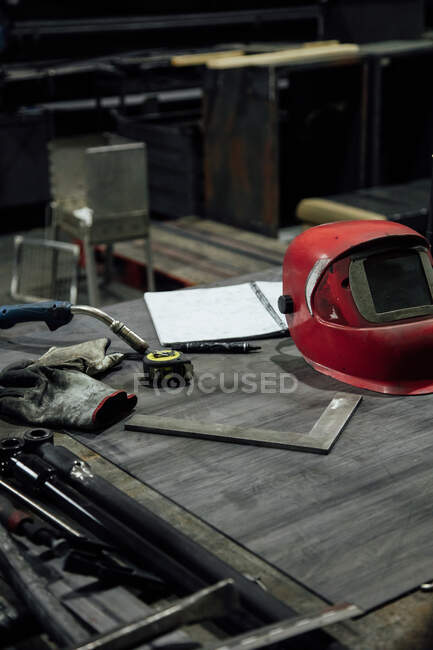 Welding mask with welding hose and gloves near notebook with pencil and measuring tape constructions on table in workshop — Stock Photo