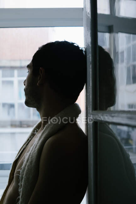 Vista lateral do homem pensativo sentado no peitoril da janela em casa — Fotografia de Stock