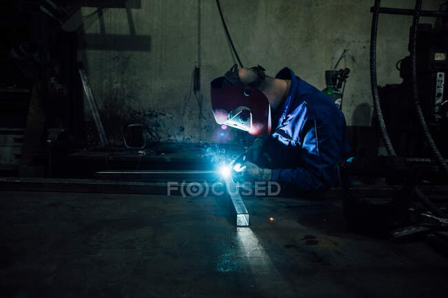 Обрізання безликого робітника в рукавичках і рівномірні деталі зварювального металу на столі поблизу будівель на заводі — стокове фото