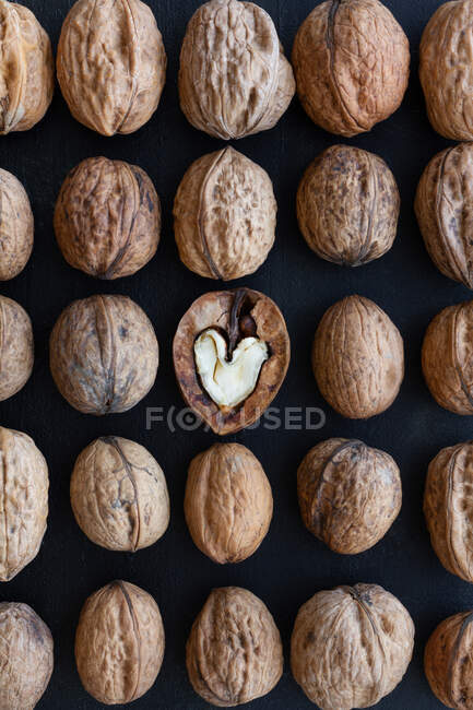 Vue du dessus de la toile de fond texturée représentant le centre de noix en forme de coeur parmi les noix entières avec des noix inégales — Photo de stock