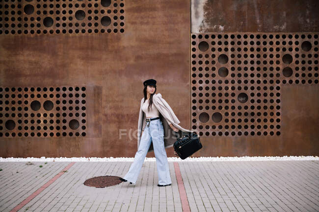 Вид сбоку на женщину-предпринимательницу в стильной одежде и с сумкой, идущую по улице в городе и отводящую взгляд — стоковое фото