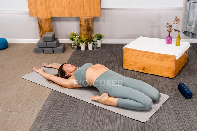 From above of flexible young female in activewear recreating in Utthita Supta Virasana pose with closed eyes while practicing yoga at home — Stock Photo