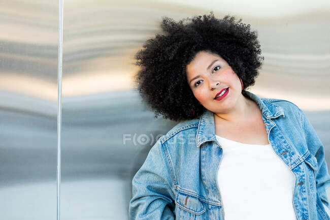 Femme adulte en surpoids dans des vêtements à la mode avec coiffure afro regardant la caméra sur fond flou — Photo de stock