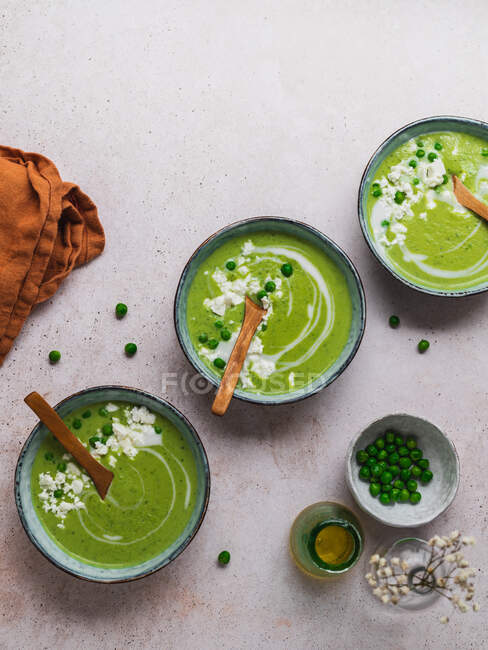 Vista superior de la deliciosa sopa de crema de guisantes en cuencos servidos en la mesa con servilleta y jarrón con flores - foto de stock