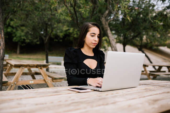 Сфокусована жінка-підприємець сидить за столом з ноутбуком в парку, працює віддалено — стокове фото