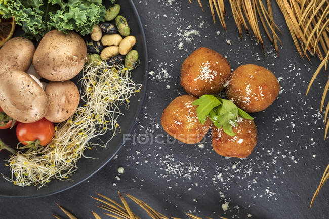 Vue de dessus des croquettes frites savoureuses avec de la poudre d'ail et des feuilles d'herbes fraîches près de l'assiette avec des légumes variés — Photo de stock