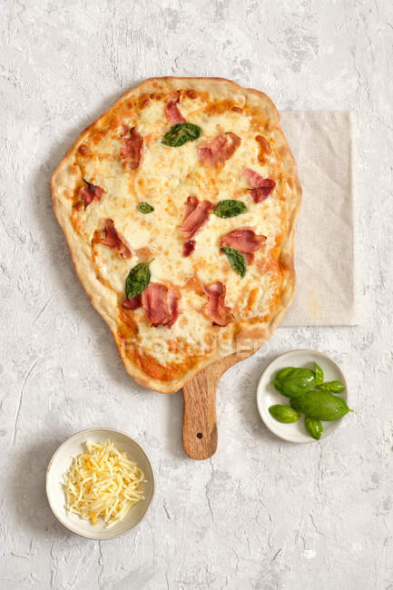 From above of tasty homemade pizza with basil and ham served on wooden cutting board on table — Stock Photo