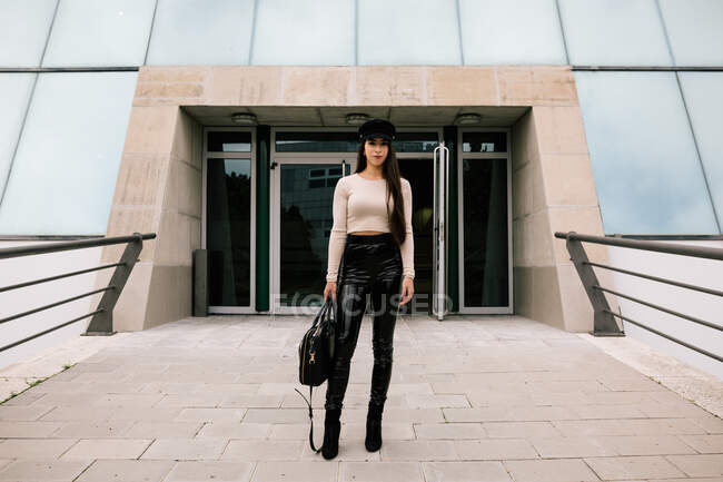 Jovem empresária na moda de pé perto da entrada do edifício contemporâneo na cidade e olhando para a câmera — Fotografia de Stock