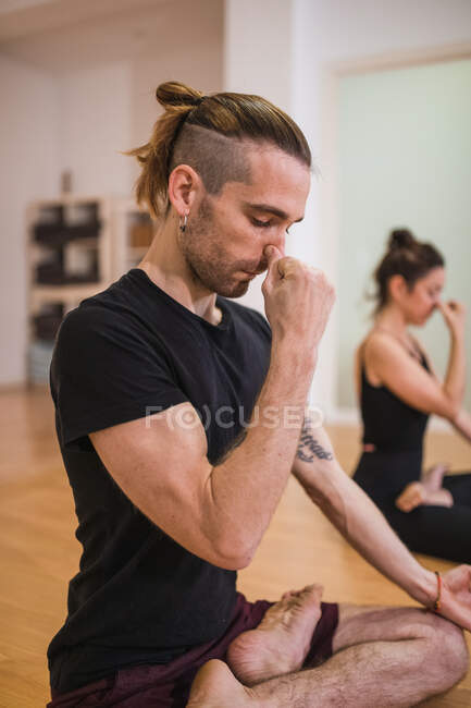 Ganzer Körper eines barfüßigen männlichen Trainers und einer Frau mit geschlossenen Augen, die Nasen kneifen, während sie Padmasana praktizieren und im Studio meditieren — Stockfoto